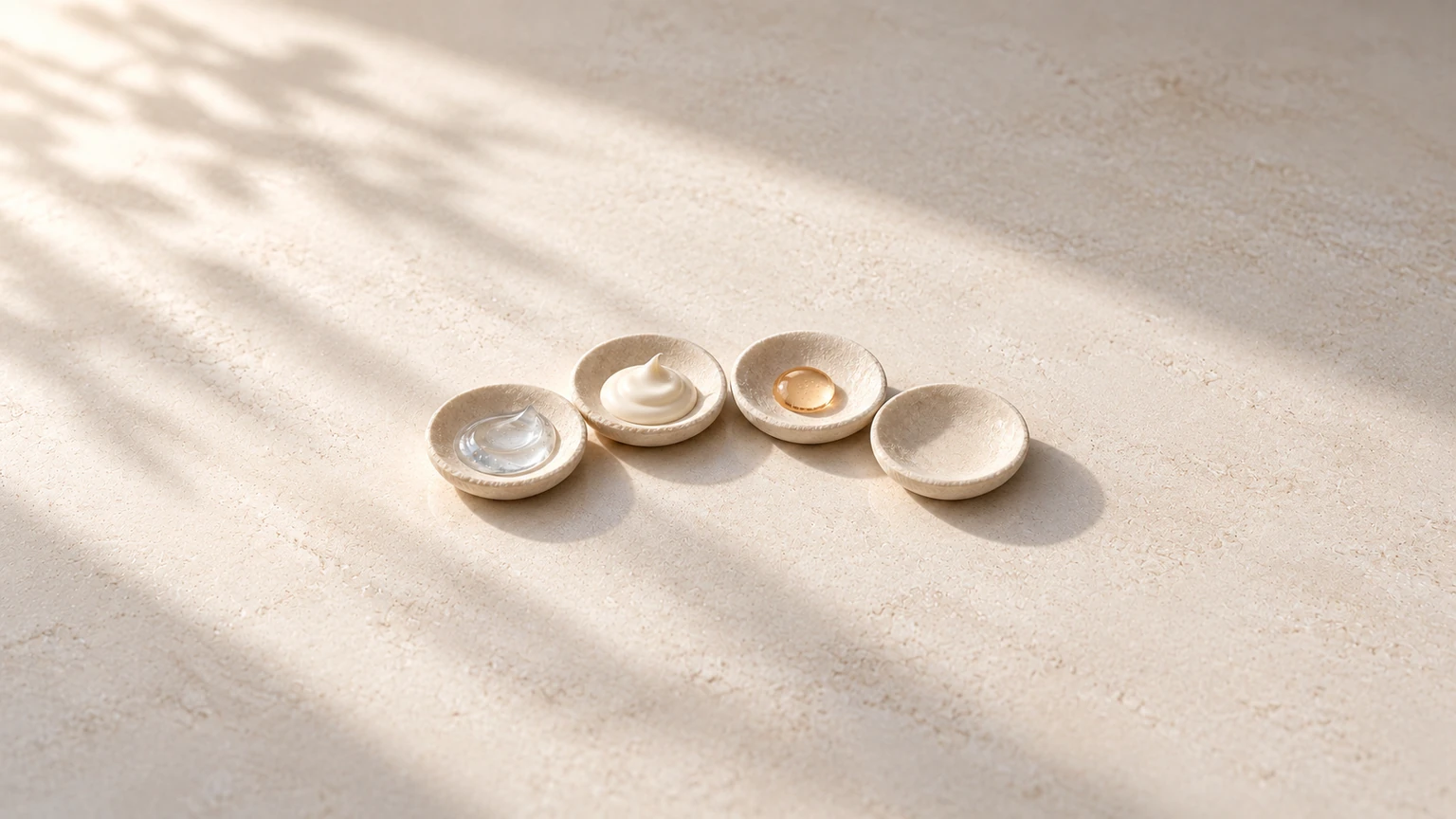 Four shallow stone dishes hold gel, cream and serum, with one dish left empty.